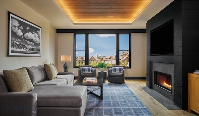 living area featuring baseboards, a tray ceiling, wooden ceiling, a fireplace, and wood finished floors