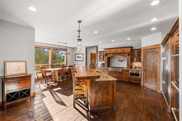 kitchen featuring brown cabinetry, glass insert cabinets, stainless steel appliances, and dark wood-type flooring