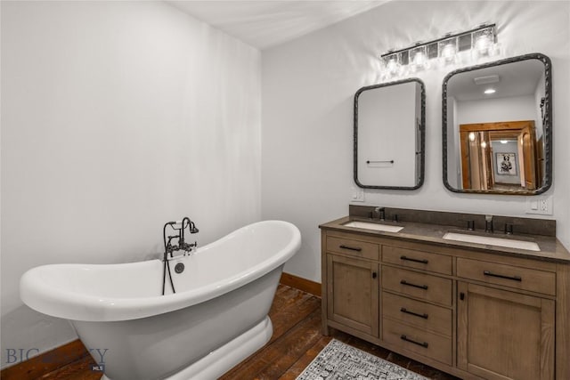 bathroom featuring double vanity, a soaking tub, wood finished floors, and a sink