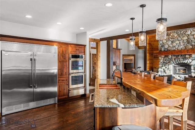 kitchen with light stone counters, dark wood-style floors, a breakfast bar, a sink, and stainless steel appliances