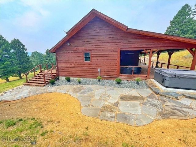 view of property exterior featuring a patio area, stairway, a deck, and a hot tub