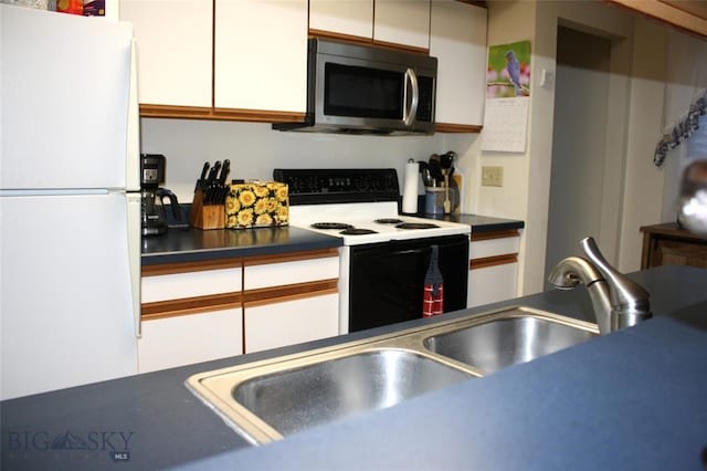 kitchen with a sink, stainless steel microwave, dark countertops, electric range oven, and freestanding refrigerator