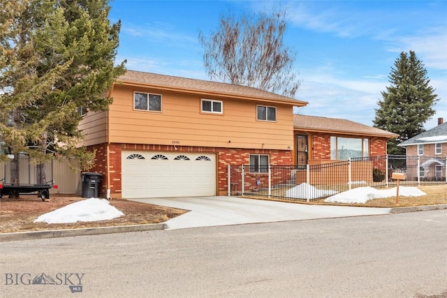 split level home featuring a garage, brick siding, driveway, and fence