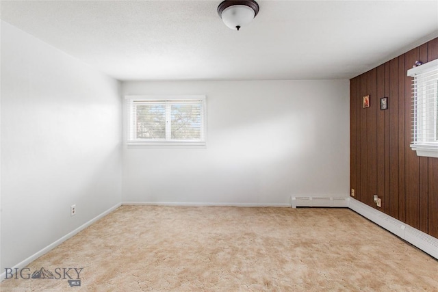 empty room featuring a baseboard heating unit, carpet floors, baseboards, and wood walls