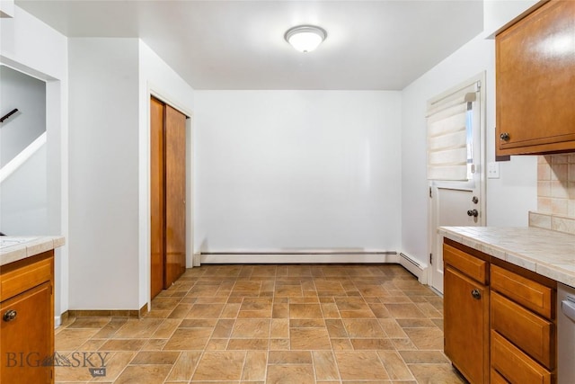 kitchen featuring tile counters, tasteful backsplash, baseboard heating, and stone finish flooring