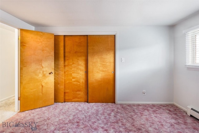 unfurnished bedroom featuring carpet, a closet, baseboard heating, and baseboards