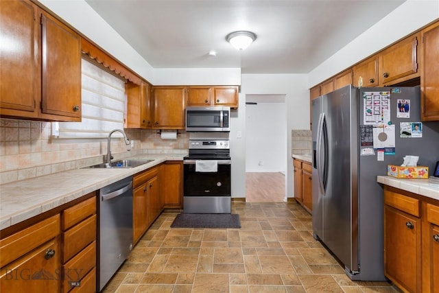 kitchen featuring backsplash, tile counters, brown cabinets, appliances with stainless steel finishes, and a sink