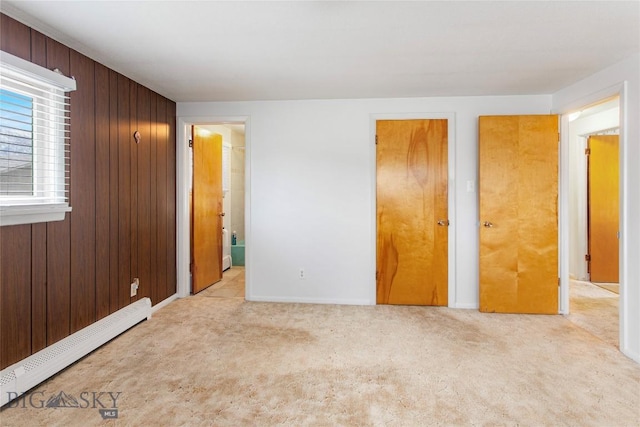 unfurnished bedroom with a baseboard heating unit, carpet flooring, and wood walls