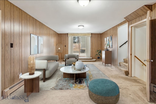 carpeted living room featuring baseboard heating, wood walls, and stairway