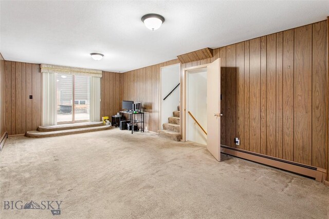 carpeted living room with stairway, a baseboard heating unit, and wood walls