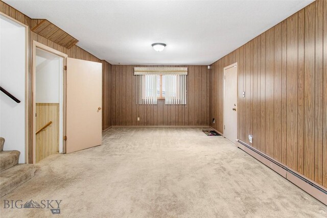 carpeted empty room with a baseboard heating unit, wooden walls, and stairway