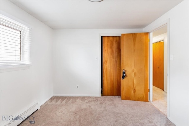 unfurnished bedroom with a closet, baseboard heating, and carpet