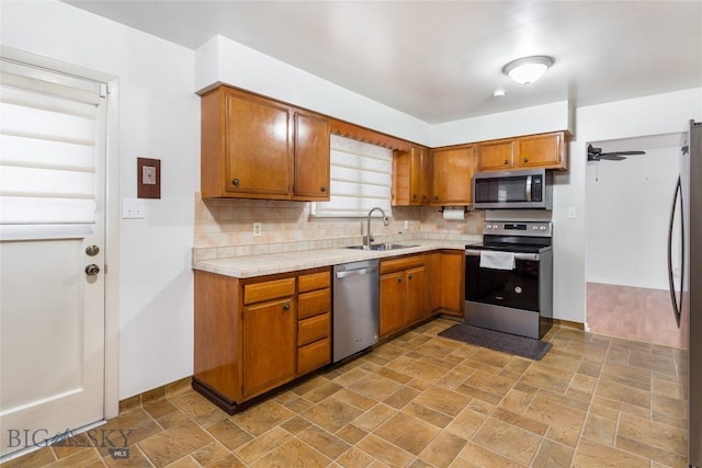 kitchen featuring decorative backsplash, brown cabinetry, stone finish floor, stainless steel appliances, and a sink