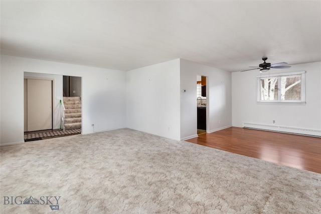 unfurnished living room featuring a baseboard radiator, ceiling fan, carpet flooring, and stairway