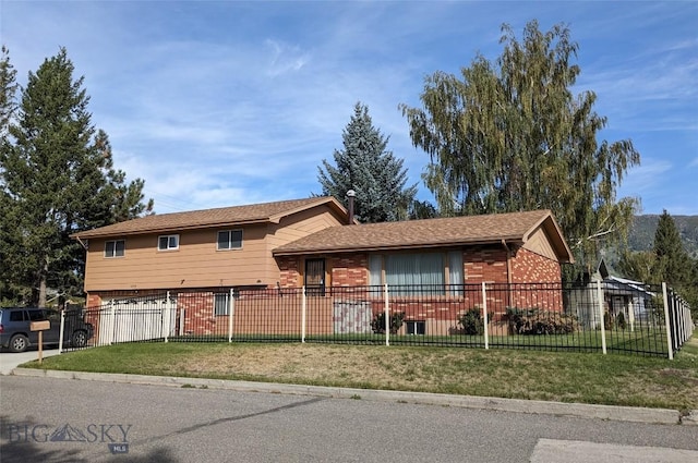 split level home with an attached garage, a fenced front yard, brick siding, a front yard, and concrete driveway