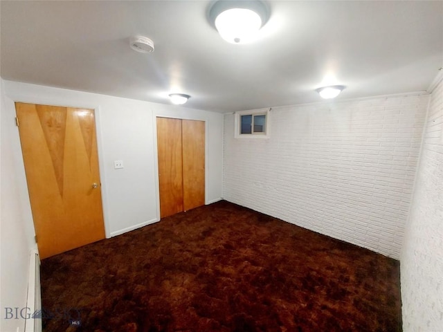 finished below grade area with brick wall, a baseboard heating unit, and dark colored carpet