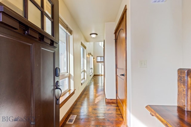 corridor featuring visible vents, baseboards, and dark wood-style flooring