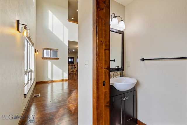 bathroom featuring visible vents, hardwood / wood-style floors, a high ceiling, baseboards, and vanity