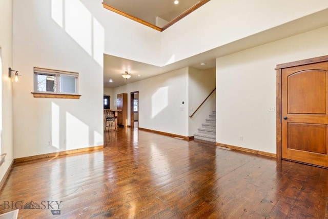 interior space featuring a towering ceiling, baseboards, hardwood / wood-style floors, and stairs