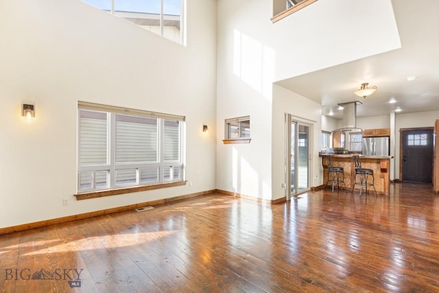 unfurnished living room featuring hardwood / wood-style floors, visible vents, baseboards, and a towering ceiling