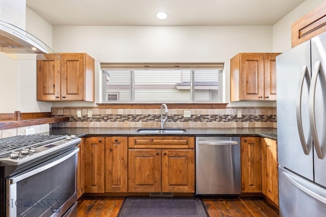 kitchen featuring a sink, dark wood-style floors, appliances with stainless steel finishes, wall chimney range hood, and decorative backsplash