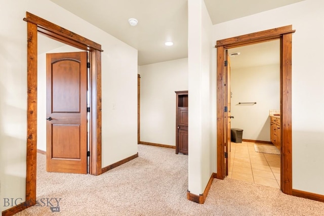 hallway with light tile patterned floors, baseboards, and light carpet