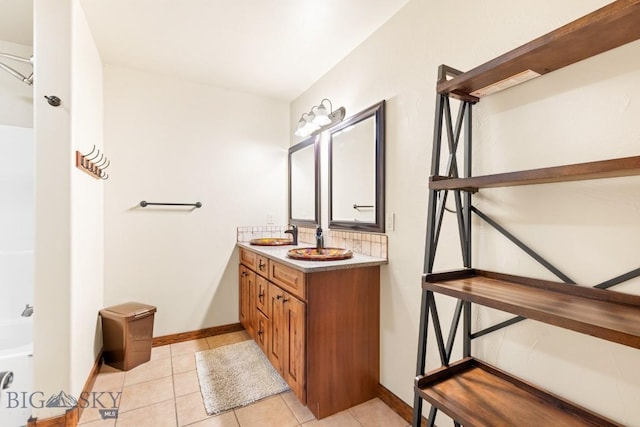 full bathroom with baseboards, double vanity, a sink, tile patterned floors, and a bathtub