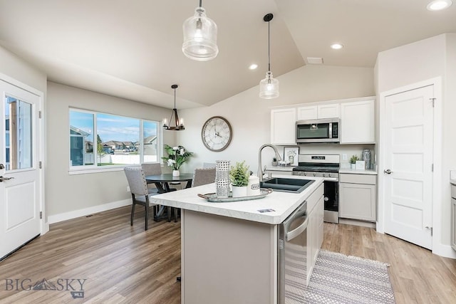 kitchen with an island with sink, a sink, stainless steel appliances, light wood-style floors, and light countertops