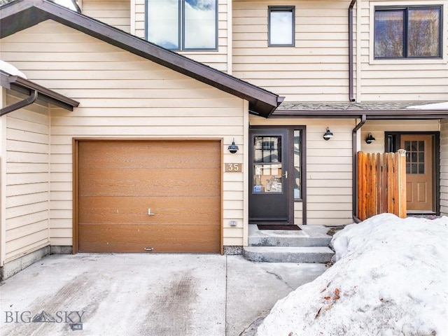 snow covered property entrance featuring concrete driveway and an attached garage