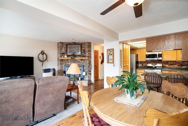 dining space with a brick fireplace, a ceiling fan, and light wood-style floors