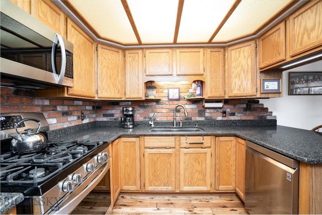 kitchen featuring a sink, light wood-style floors, appliances with stainless steel finishes, and dark stone countertops