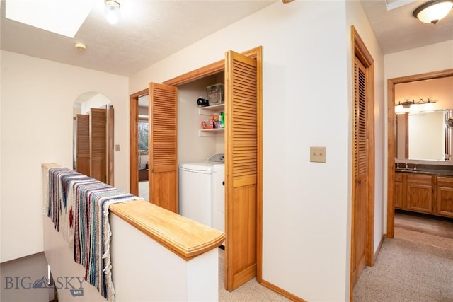 corridor featuring a skylight, baseboards, light colored carpet, and washing machine and dryer