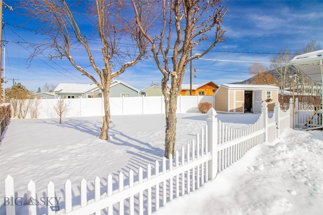 yard covered in snow featuring an outbuilding, a fenced backyard, and a residential view