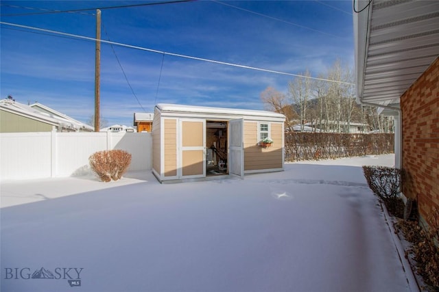 snow covered patio with a storage shed, an outbuilding, and a fenced backyard