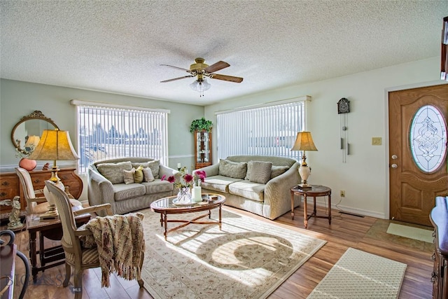 living area with wood finished floors, visible vents, a ceiling fan, baseboards, and a textured ceiling