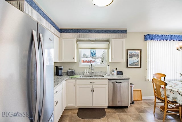 kitchen with a sink, light stone counters, appliances with stainless steel finishes, white cabinets, and baseboards