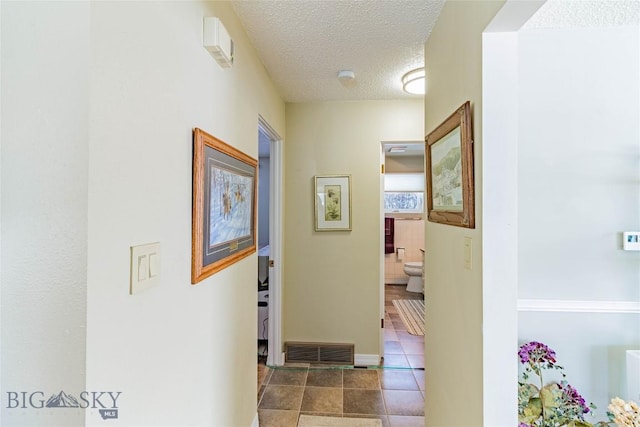 hall featuring tile patterned floors, visible vents, baseboards, and a textured ceiling