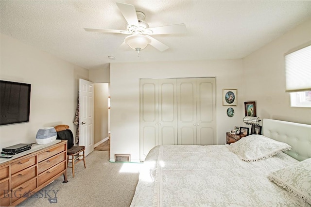 bedroom featuring a textured ceiling, light colored carpet, a closet, and ceiling fan