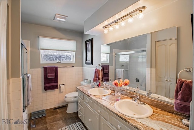 full bathroom with double vanity, a shower stall, tile walls, and a sink