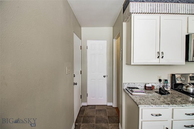 kitchen with stainless steel microwave, white cabinets, baseboards, and light stone countertops