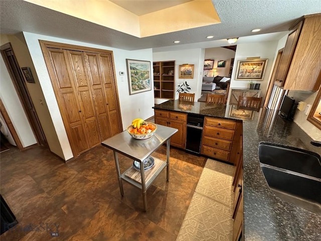 kitchen featuring dark stone countertops, a peninsula, a sink, a textured ceiling, and brown cabinets