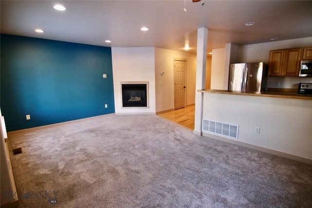 unfurnished living room featuring recessed lighting, visible vents, light carpet, and a glass covered fireplace