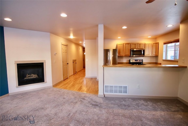 kitchen featuring visible vents, recessed lighting, appliances with stainless steel finishes, a glass covered fireplace, and light colored carpet