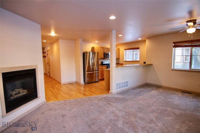 unfurnished living room featuring a wealth of natural light, visible vents, light colored carpet, and a glass covered fireplace