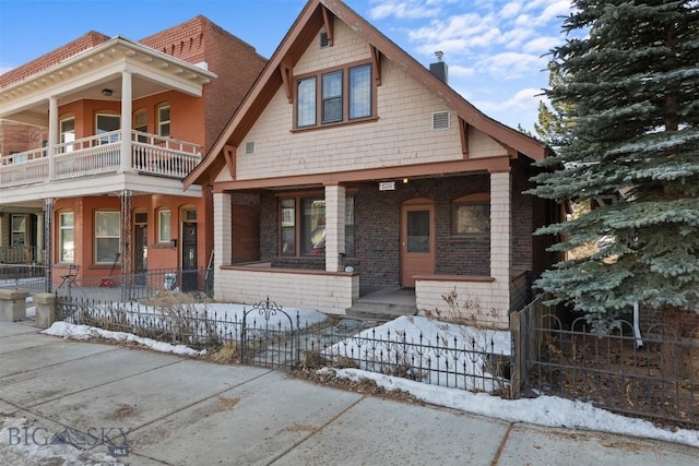 view of front of home with a fenced front yard, a balcony, covered porch, brick siding, and a chimney