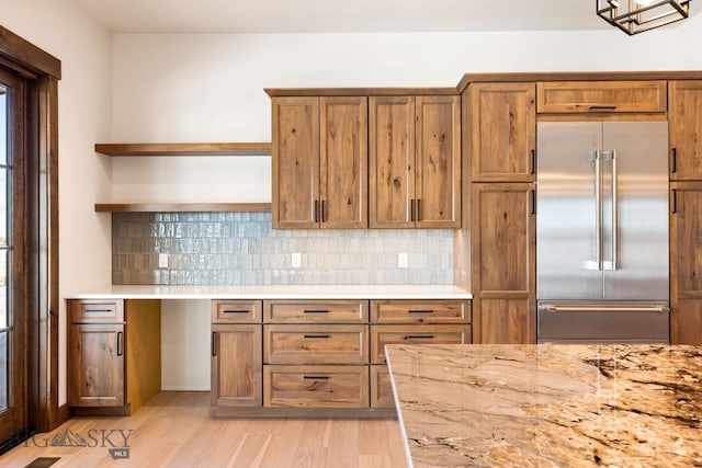 kitchen featuring stainless steel built in refrigerator, open shelves, tasteful backsplash, light wood-style floors, and brown cabinetry