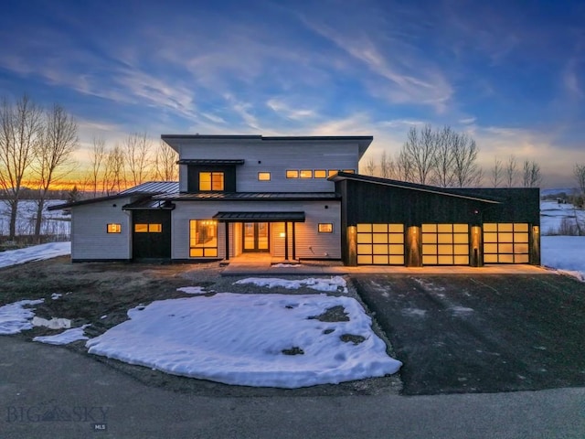 modern home with metal roof, aphalt driveway, an attached garage, and a standing seam roof