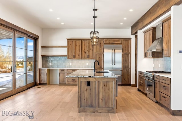 kitchen featuring light stone countertops, high quality appliances, light wood-style flooring, a sink, and wall chimney exhaust hood