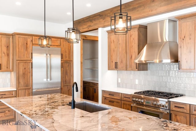 kitchen with a sink, premium appliances, light stone counters, backsplash, and wall chimney range hood