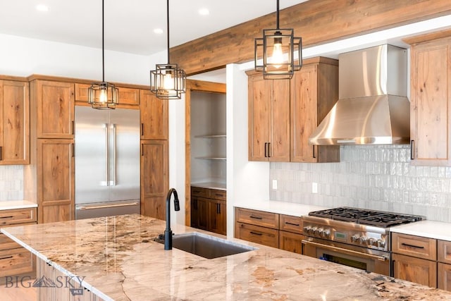 kitchen with decorative backsplash, a sink, light stone counters, wall chimney range hood, and premium appliances